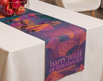 May include: A rectangular table runner featuring a vibrant, colorful illustration of a landscape with trees and a tent. The text "HAPPY FEAST OF TABERNACLES" and "LEVITICUS 23:33-44" is printed in gold lettering at the bottom of the fabric runner.