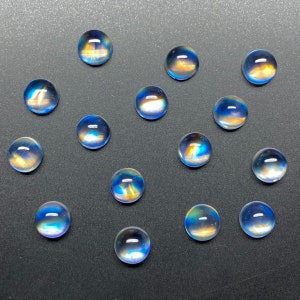 May include: A collection of 15 iridescent blue and gold moonstone cabochons. The cabochons are round and have a smooth, polished surface.