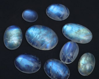 May include: A collection of nine oval-shaped moonstone cabochons with iridescent blue and white colors. The stones are arranged on a black background.