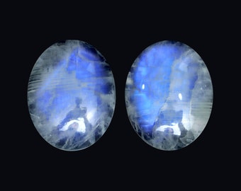 May include: Two oval-shaped moonstone cabochons with a blue iridescent sheen. The stones are translucent and have a white base.