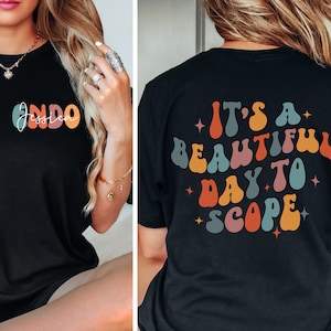 May include: Black t-shirt with a colorful retro design on the back that says "It's a beautiful day to scope". The front of the shirt has a colorful retro design with the name "Jessica" written in white.