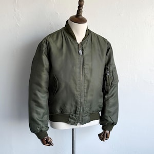 Puede incluir: Una chaqueta bomber de color verde oliva con cremallera frontal completa, cuello, puños y dobladillo acanalados. La chaqueta incluye un bolsillo utilitario con cierre de cremallera en la manga izquierda y dos bolsillos laterales con botones.