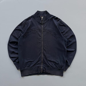 May include: A dark navy blue zip-up jacket featuring a high collar and long sleeves. The word BURBERRY is embroidered in a matching dark navy thread across the chest in an arched design. The jacket includes a central metal zipper closure.