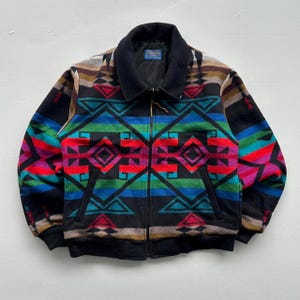 May include: A colorful, patterned jacket with a black collar and zipper. The jacket features a geometric design in shades of red, blue, green, and black. The jacket has a black ribbed hem and cuffs.