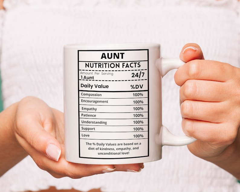 May include: White ceramic mug with a black and white design that reads "Aunt Nutrition Facts" with a list of positive qualities and their percentage daily value. The mug is held by a person's hands.