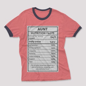 May include: A red t-shirt with a black and navy blue ringer. The shirt features a white graphic of a nutrition facts label with the title "AUNT" and the text "24/7". The label lists various qualities of an aunt, such as compassion, encouragement, empathy, patience, understanding, support, and love, all with a value of 100%.