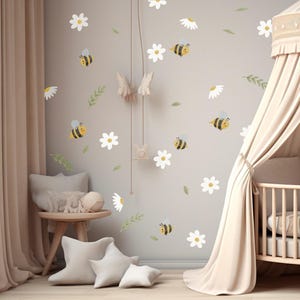 Op de afbeelding: Een set muurstickers met cartoonbijen, witte madeliefjes en groene blaadjes op een lichtgrijze muur. De stickers bevatten diverse geel-zwart gestreepte bijen met blauwe vleugels, witte bloesems en kleine groene takjes als decoratie.