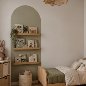 Könnte beinhalten: Kinderzimmer mit hellgrüner Akzentwand und Holzregalen mit Büchern. Ein Holzbett mit einer grünen Steppdecke und einem Weidenkorb mit einem Stofftier sind ebenfalls zu sehen. Eine gewebte Leuchte hängt von der Decke.