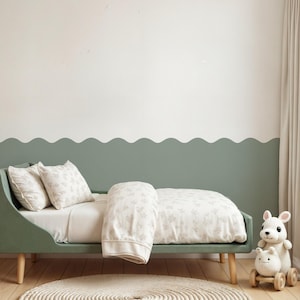 Peut inclure: Un lit d'enfant avec un cadre vert sauge et des pieds en bois clair. Le lit est fait avec un drap blanc, une housse de couette à motifs et deux oreillers assortis. Une peluche et un jouet en bois sont placés à côté du lit. Un tapis rond et tissé est au sol.
