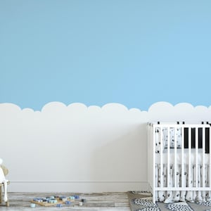 May include: A white crib with a black and white star patterned blanket, positioned against a wall featuring a light blue upper section and a white cloud-shaped border. A white rabbit figurine sits on a small wooden chair nearby on the floor.