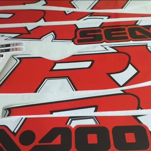 Peut inclure: Graphiques de moto rouge et blanc avec inscription noire "SE400" et "RY" avec un contour blanc. Les graphiques sont sur un fond blanc.