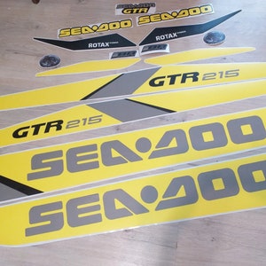 以下が含まれることがあります： 黄色と灰色のSea-Doo GTR 215のデカールセット。デカールにはSea-Dooのロゴと「GTR 215」の文字が書かれています。