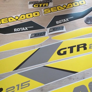 以下が含まれることがあります： 黄色と黒のSea-Doo GTR 215デカールセット。デカールには、Sea-Dooロゴ、GTR 215モデル名、Rotax Powerロゴが描かれています。