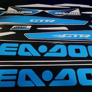 May include: A set of black and blue Sea-Doo GTR decals with the text "Sea-Doo" and "GTR" in a bold, white font. The decals are designed for a Sea-Doo watercraft.