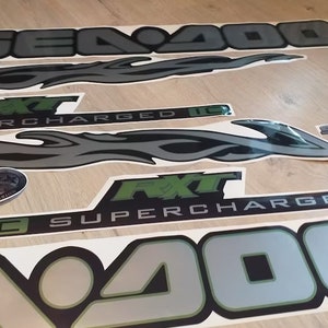 May include: A set of black and silver decals with green accents. The decals feature the words "Sea-Doo", "FXT", "Supercharged", and "Tec" along with a flame design.