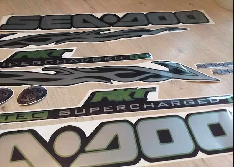 May include: A set of black and silver decals with green accents. The decals feature the words "Sea-Doo", "FXT", "Supercharged", and "Tec" along with a flame design.