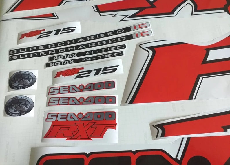 Peut inclure: Un ensemble d'autocollants noirs et blancs avec des accents rouges pour un bateau Sea-Doo. Les autocollants comprennent le texte "RXT 215", "SUPERCHARGED", "ROTAX 4-TEC" et "SEA-DOO".
