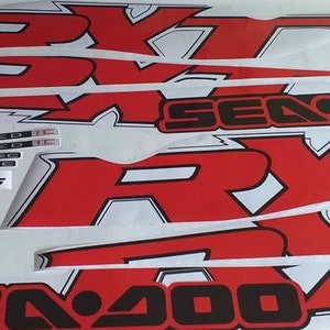 Peut inclure: Un ensemble d'autocollants Sea-Doo RX-T rouges et noirs avec le texte "Sea-Doo" et "RX-T" en noir. Les autocollants comprennent &eacute;galement le texte "215 Supercharged" et "Rotax 4-Tec".