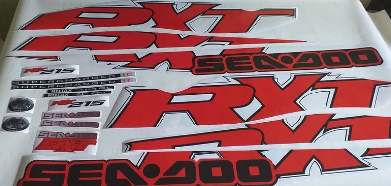 Peut inclure: Un ensemble d'autocollants Sea-Doo RX-T rouges et noirs avec le texte "Sea-Doo" et "RX-T" en noir. Les autocollants comprennent &eacute;galement le texte "215 Supercharged" et "Rotax 4-Tec".