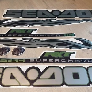 May include: A set of black and silver Sea-Doo decals with green accents. The decals include the words "Sea-Doo", "4-Tec Supercharged", and "R.X.T."
