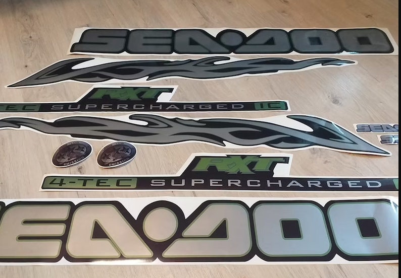 May include: A set of black and silver Sea-Doo decals with green accents. The decals include the words "Sea-Doo", "4-Tec Supercharged", and "R.X.T."