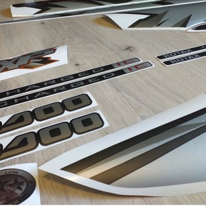 Puede incluir: Un conjunto de calcoman&iacute;as negras y plateadas para un veh&iacute;culo. Las calcoman&iacute;as incluyen las palabras "Charged" y "400" en una fuente en negrita. Tambi&eacute;n hay dos calcoman&iacute;as con la palabra "Rotax" y el texto "4-Tec" y "4-Tec-E".