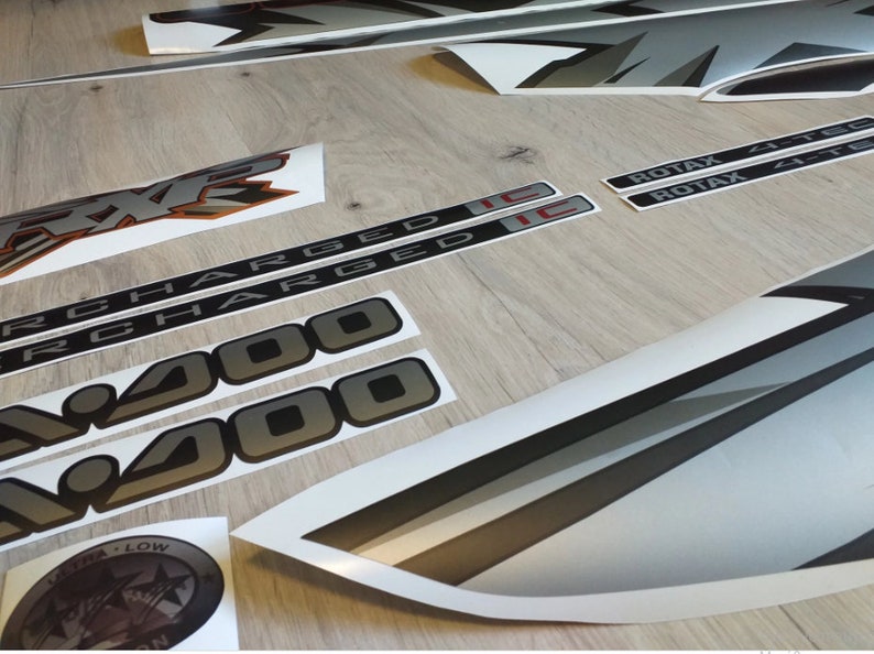 Puede incluir: Un conjunto de calcoman&iacute;as negras y plateadas para un veh&iacute;culo. Las calcoman&iacute;as incluyen las palabras "Charged" y "400" en una fuente en negrita. Tambi&eacute;n hay dos calcoman&iacute;as con la palabra "Rotax" y el texto "4-Tec" y "4-Tec-E".