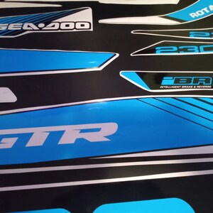 May include: A set of black and white decals with blue accents for a Sea-Doo watercraft. The decals feature the text "Sea-Doo", "GTR", "230", "ROTAX", and "iBR Intelligent Brake & Reverse".