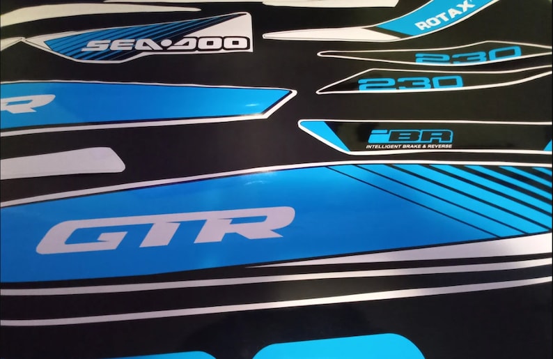 May include: A set of black and white decals with blue accents for a Sea-Doo watercraft. The decals feature the text "Sea-Doo", "GTR", "230", "ROTAX", and "iBR Intelligent Brake & Reverse".