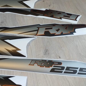 Puede incluir: Un conjunto de calcoman&iacute;as de motocicleta negras y plateadas con el texto "RXP 255" y un dise&ntilde;o gr&aacute;fico estilizado. Las calcoman&iacute;as est&aacute;n sobre un fondo blanco.