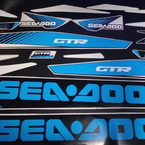 May include: A set of blue and white Sea-Doo GTR 230 decals. The decals feature the Sea-Doo logo, the model name, and the engine size. The decals are designed to be applied to a Sea-Doo watercraft.