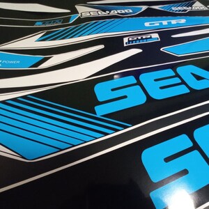 May include: A set of blue and white vinyl decals with the words "Sea-Doo" and "GTX" printed on them. The decals are designed for a watercraft.