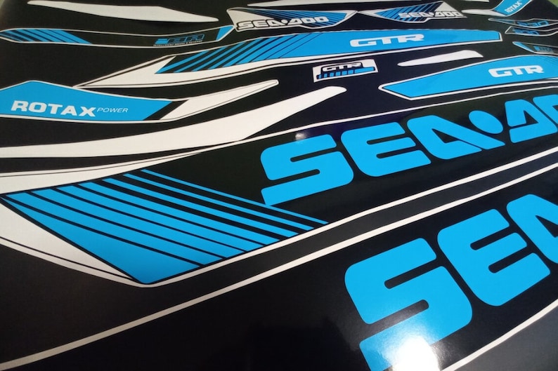 May include: A set of blue and white vinyl decals with the words "Sea-Doo" and "GTX" printed on them. The decals are designed for a watercraft.