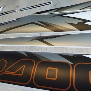 Puede incluir: Un conjunto de calcoman&iacute;as de vinilo en blanco y negro con un dise&ntilde;o gris y naranja. Las calcoman&iacute;as presentan la palabra "400" en una fuente negrita y estilizada.