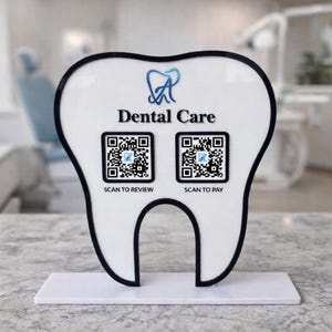May include: A white, tooth-shaped sign with black trim and a white base. The sign features the words "Dental Care" and two QR codes labeled "Scan to Review" and "Scan to Pay". A dental logo is at the top.
