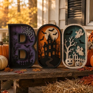 Pode incluir: Três placas decorativas de madeira que formam a palavra BOO, com recortes em camadas de uma teia de aranha, uma casa assombrada com lua cheia e fantasmas em um cemitério. As letras são emolduradas em preto e têm fundos coloridos.