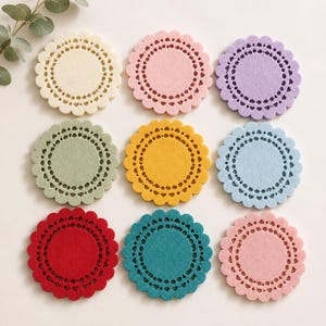 May include: Nine colorful felt coasters in a variety of colors, including cream, pink, purple, green, yellow, blue, red, teal, and light pink. Each coaster has a scalloped edge and a decorative, perforated inner circle.