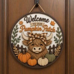 May include: A round wooden wall sign featuring a layered design of a highland cow wearing a brown and white plaid bow. The text reads Welcome to our Pumpkin Patch. The sign includes orange, green, and cream pumpkins, a fence, and autumn leaves.