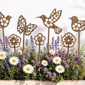 Può includere: Un set di sei picchetti da giardino in legno marrone con disegni tagliati al laser di due uccelli, un colibrì, una farfalla e due fiori, inseriti in una fioriera rettangolare in legno riempita di lavanda viola e margherite bianche.