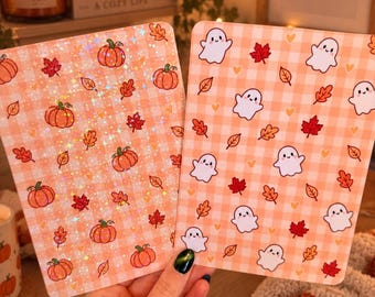 May include: Two rectangular cards with rounded corners featuring autumn themes. The left card has a holographic finish with orange pumpkins and red and orange leaves on a light orange gingham background. The right card shows white ghosts, red and orange leaves, and small yellow hearts on a light orange gingham background.