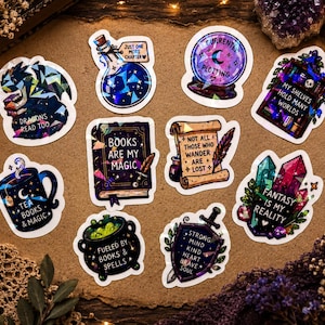 May include: A collection of ten die-cut stickers featuring fantasy themes, including a dragon, potion bottle with text 'JUST ONE MORE CHAPTER', crystal ball with 'CURRENTLY PLOTTING', bookshelf, mug, book, scroll, cauldron, shield, and crystals.