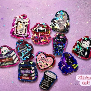 May include: A set of colourful stickers featuring diverse designs and text, such as a coffin, a vampire, a skull, and a coffee cup. The stickers have a glittery, holographic effect and are set against a purple background.