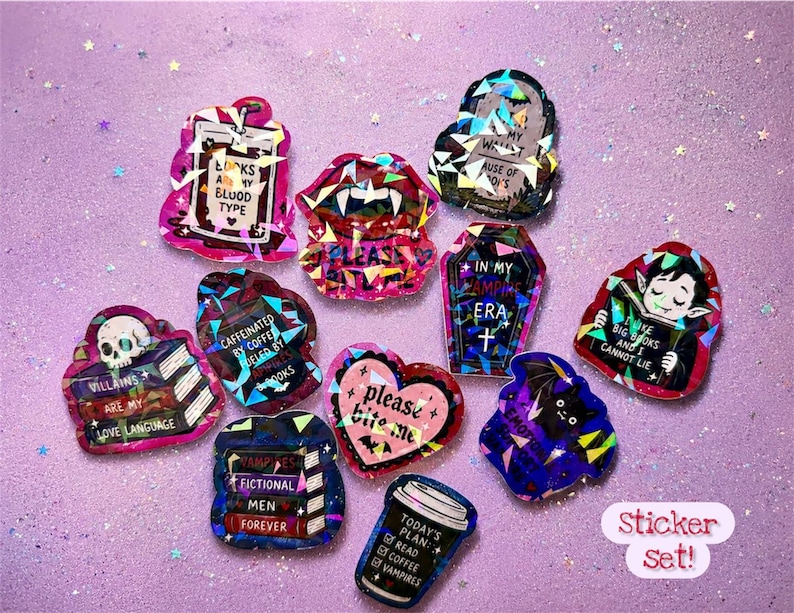 May include: A collection of colorful stickers with various designs and text, including a coffin, a vampire, a skull, and a coffee cup. The stickers have a glittery, holographic effect and are set against a purple background.