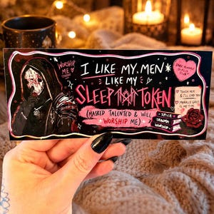 May include: A black and pink Sleep Token sticker with the text "I Like My Men Like My Sleep Token". The sticker features an illustration of a figure in a hooded cloak and a skull mask. Additional text includes "Dark Romance Girlie Club".
