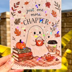 May include: A rectangular holographic sticker featuring a ghost holding a red mug, a pumpkin, a stack of books labelled Spooky Stories & Coffee, and a cup labelled pumpkin spice. The text reads just one more CHAPTER amidst autumn leaves.