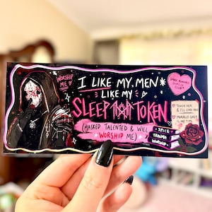 May include: A rectangular sticker with a black background and pink and white text. The sticker features an illustration of a figure in a hooded cloak and the text "I LIKE MY MEN LIKE MY SLEEP TOKEN". Additional text includes "Worship Me" and "Dark Romance Girlie Club".
