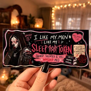 May include: A black rectangular sticker with white and pink text and illustrations. The text reads "I like my men like my sleep token." A hooded figure with a mask is on the left. The sticker also has the words "Dark Romance Girlie Club."