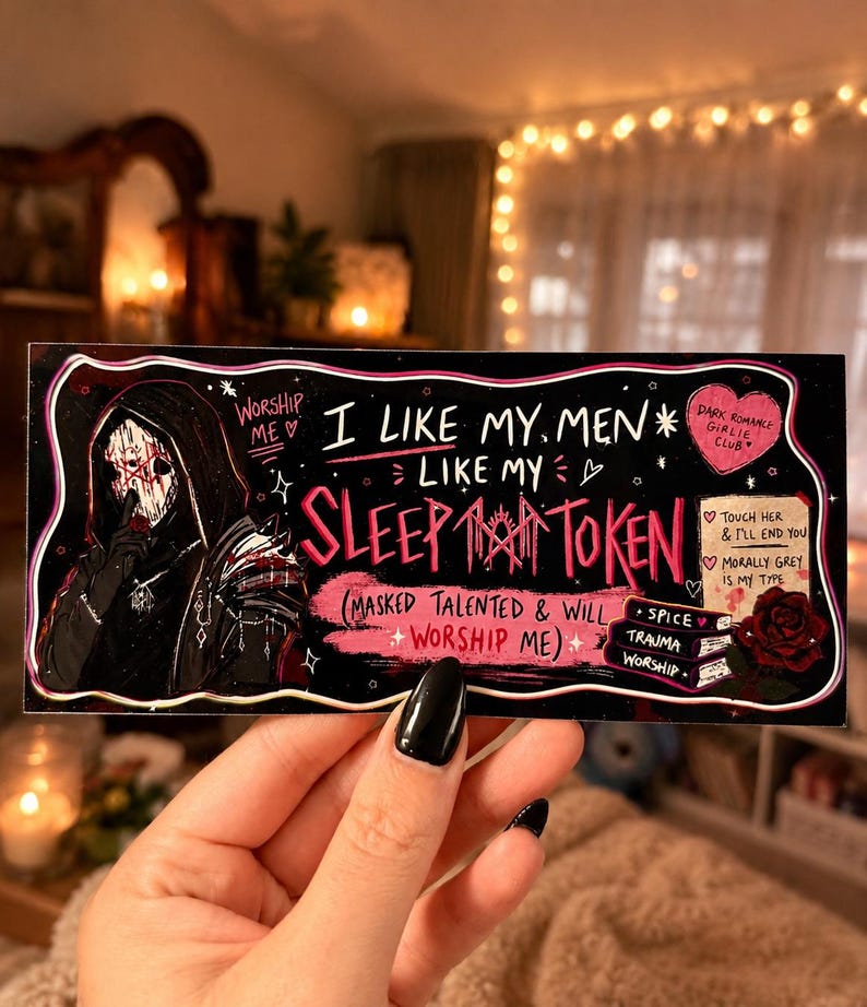 May include: A black rectangular sticker with white and pink text and illustrations. The text reads "I like my men like my sleep token." A hooded figure with a mask is on the left. The sticker also has the words "Dark Romance Girlie Club."
