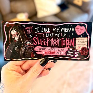 May include: A black sticker with pink and white text and illustrations. The text reads "I like my men like my sleep token." A masked figure is on the left. Other text includes "Dark Romance Girlie Club."