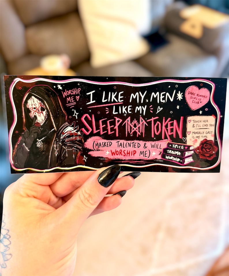 May include: A black sticker with pink and white text and illustrations. The text reads "I like my men like my sleep token." A masked figure is on the left. Other text includes "Dark Romance Girlie Club."
